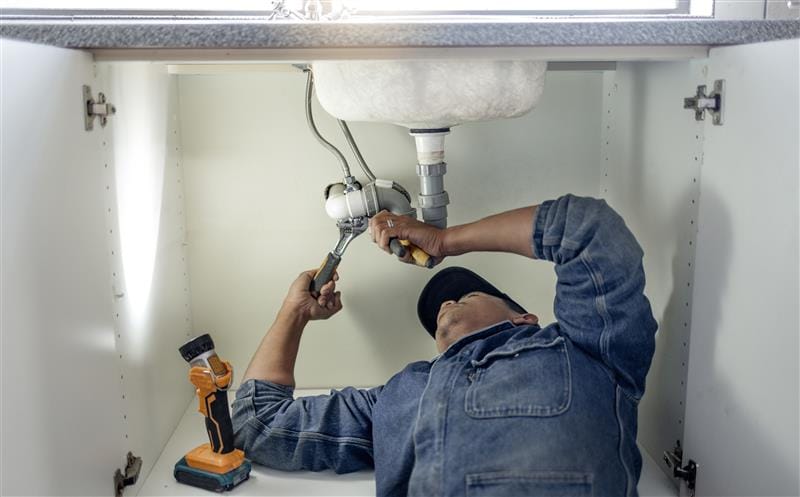 Plumber repairing pipes beneath a bathroom sink in Downey